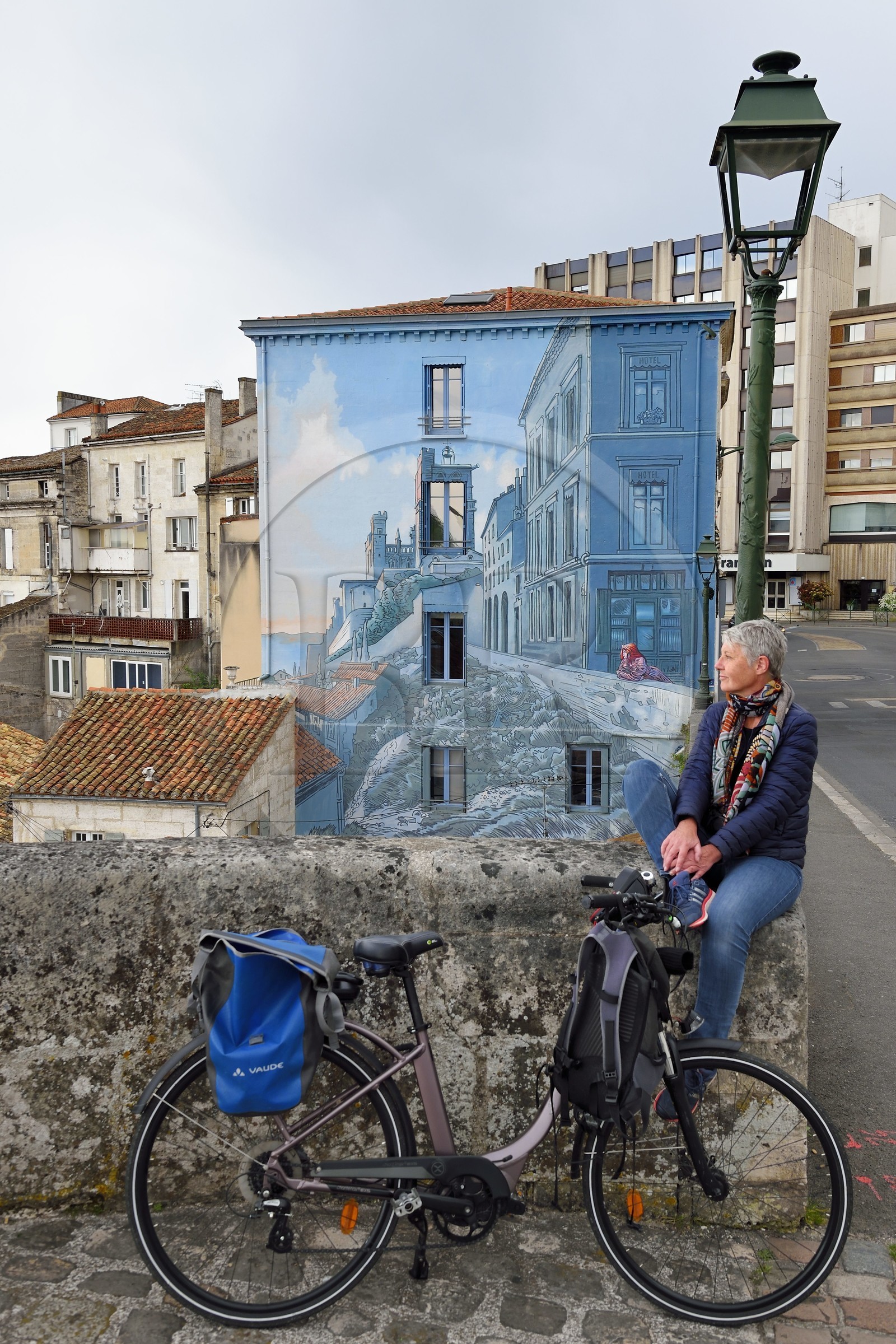 France, Charente, Angouleme, Boulevard Pasteur in the historic center, cyclist doing the cycle route La Flow Vélo in front of La fille des Remparts, painted wall from an original drawing by Max Cabanes and made by the Cité de la Création in 2004