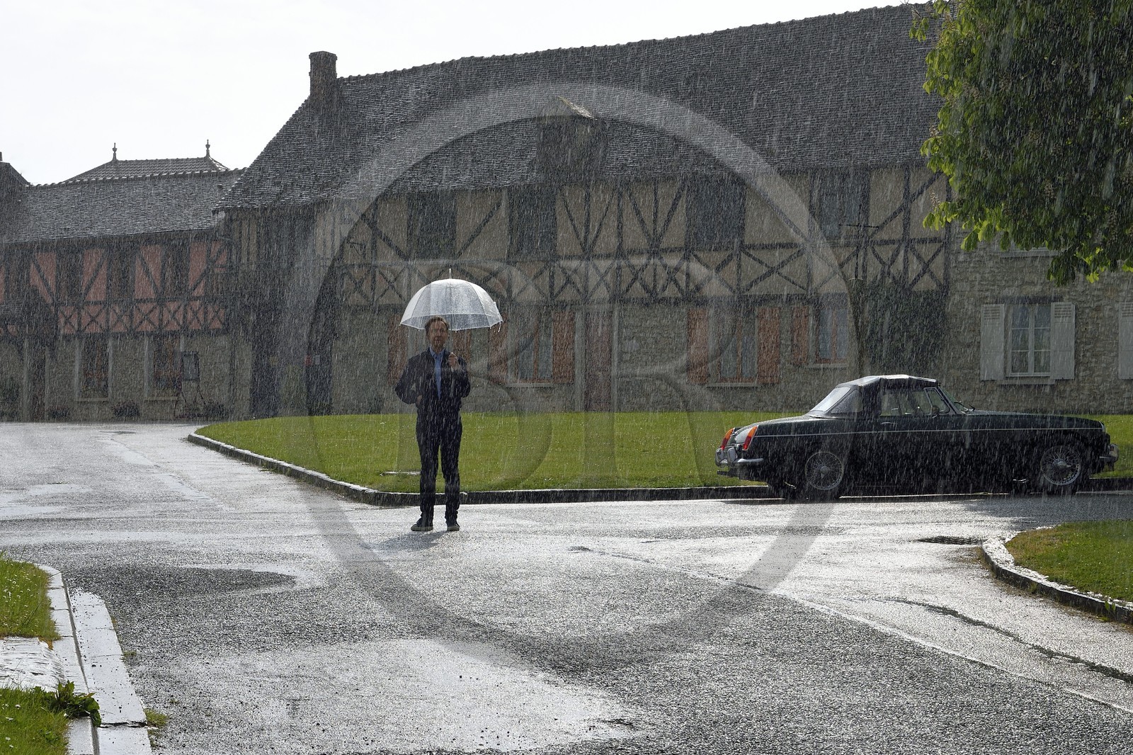 France, Yvelines (78), Montchauvet, tournage pour la télévision du Village Préféré des Français avec Stéphane Bern, Stéphane Bern sous la pluie sur la place de l'église