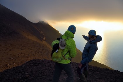 Italie, Sicile, iles Eoliennes, classées Patrimoine Mondial de l'UNESCO, ile de Stromboli, randonneurs observant les fumerolles sur les pentes du volcan actif au coucher de soleil