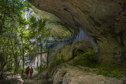 France, Vaucluse, Mont Ventoux Regional Natural Park, Monieux, Gorges de La Nesque, hikers walking under a rock ledge at the bottom of the canyon towards the 12th century Saint-Michel chapel
