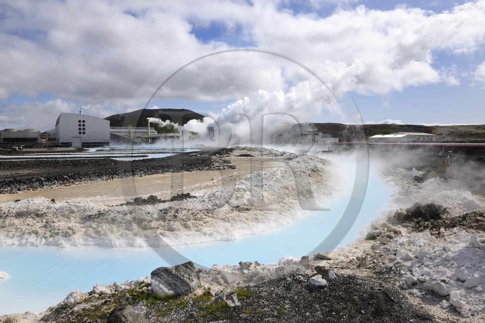 Iceland, Sudurnes Region, Grindavik, the Blue Lagoon with drains and lava in the foreground and the geothermical factory in the background