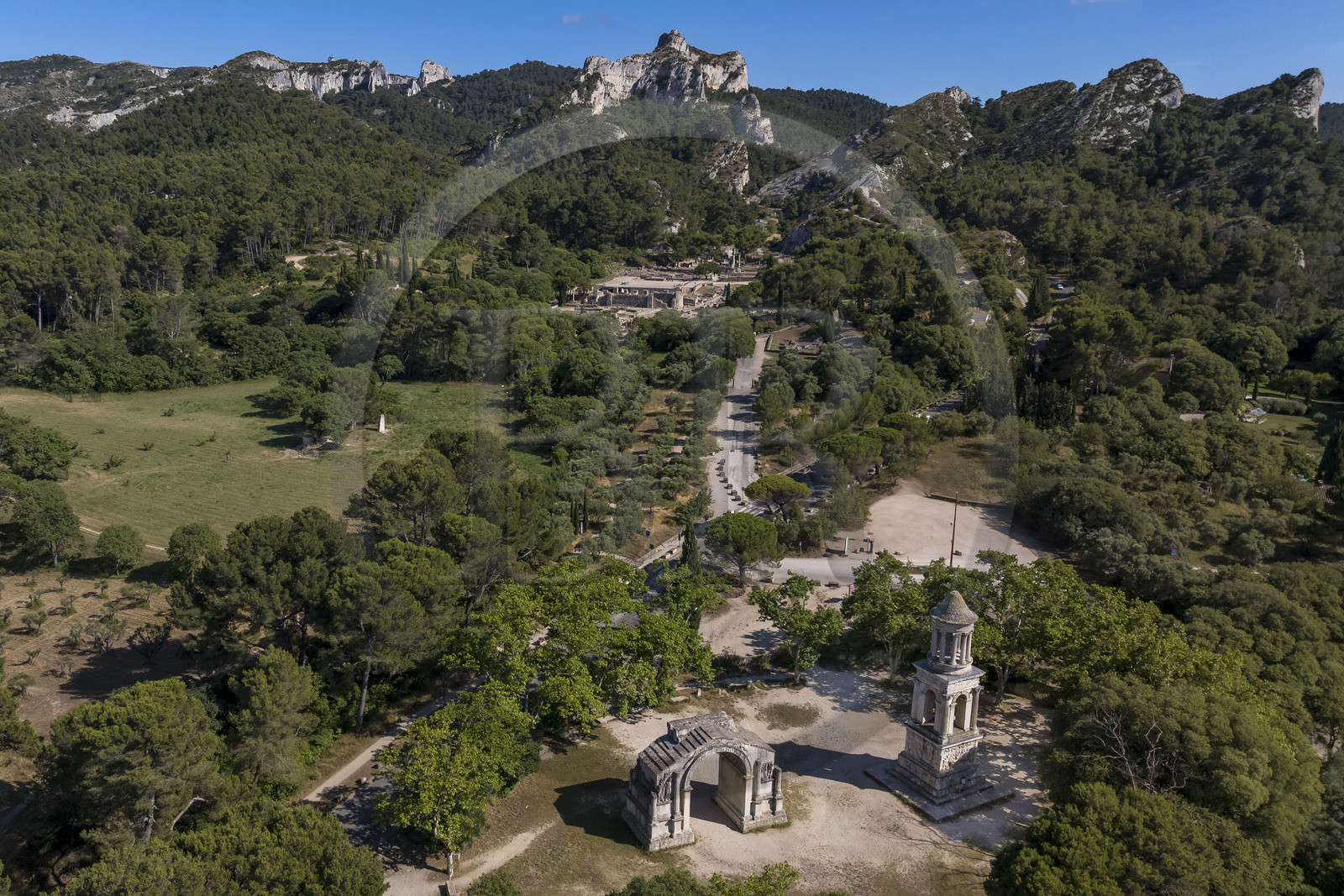 France, Bouches du Rhone, Regional Natural Park of the Alpilles, Saint Remy de Provence, les Antiques de Glanum, Gallo-Roman cenotaph erected between -30 and -20 BC in memory of a man from the Julii family and municipal arch of Glanum (Roman triumphal arch), the archaeological site of Glanum in the background (aerial view)