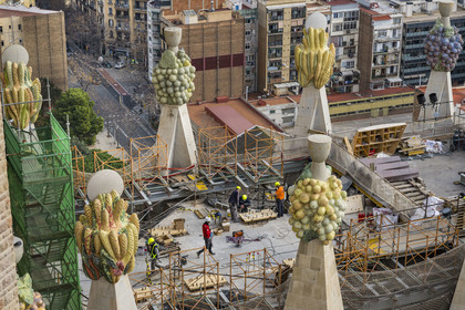 Spain, Catalonia, Barcelona, Eixample district, Sagrada Familia basilica by Catalan modernist architect Antoni Gaudi, listed as a UNESCO World Heritage Site, peaks topped with mosaics in the shape of fruits surrounding the construction site on the roof of the nave at the rear of the future facade of the Glory