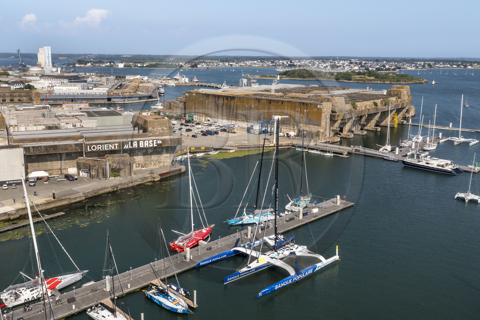 France, Morbihan (56), Lorient, le port de Lorient La Base dans l'ancienne base de sous-marins construite par les Allemands, il est conçu et équipé de façon à accueillir les professionnels du nautisme, les événements nautiques et les grandes unités telles que les monocoques et les multicoques de la Course au Large, voilier maxi-trimaran-hydroptère Maxi Banque populaire XI du navigateur Armel Le Cléac'h (vue aérienne)