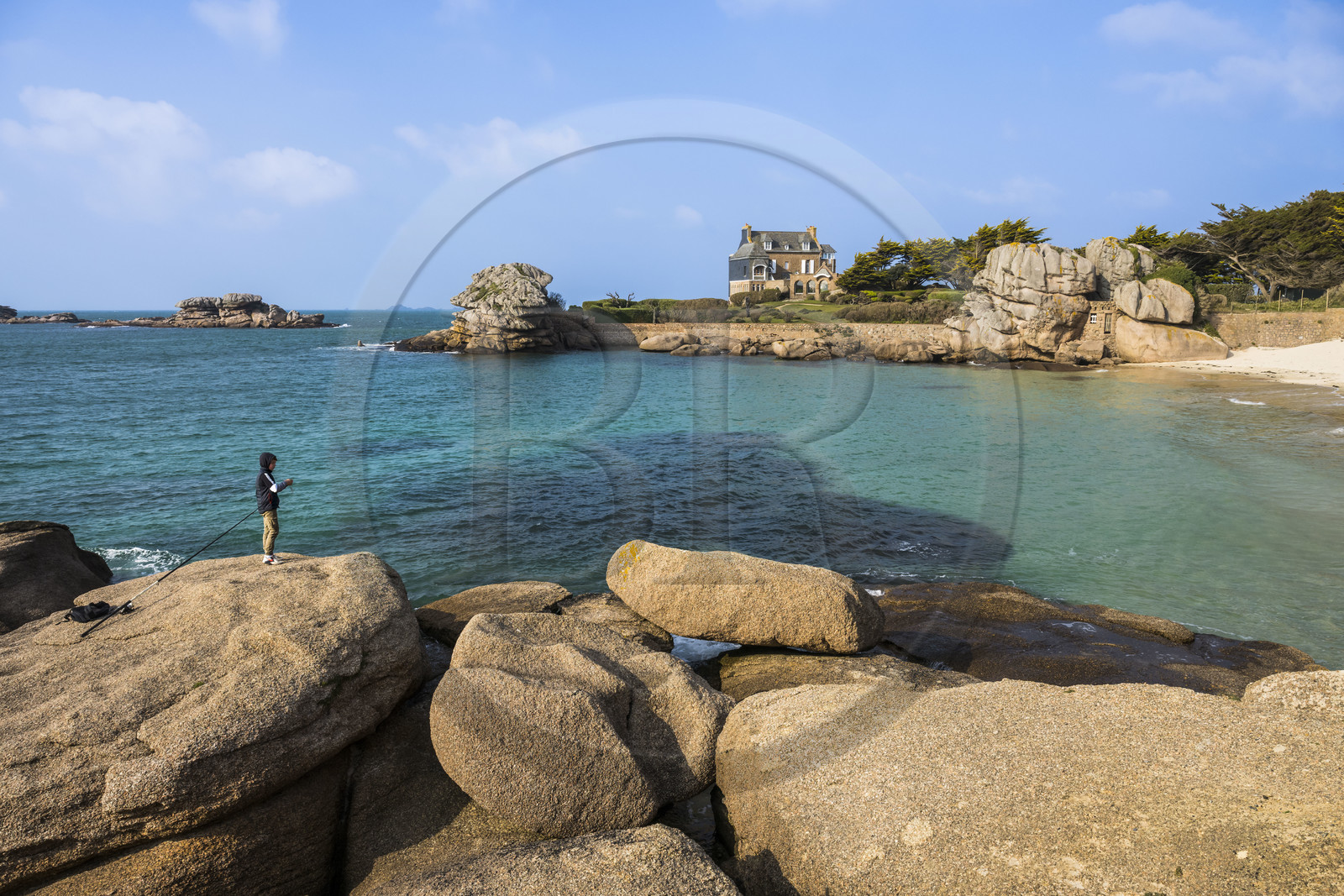 France, Côtes-d'Armor (22), Côte de Granit Rose, Trégastel, jeune pecheur à la ligne sur les rochers devant la plage de Ker ar Vir que longe le chemin de Grande Randonnée GR 34, maison de la famille Roux en arrière plan