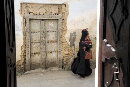 Tanzanie, archipel de Zanzibar, île de Unguja (Zanzibar), ville de Zanzibar, quartier Stone Town, classé Patrimoine Mondial de l' UNESCO, femme voilée passant devant une porte de type arabe de la vieille ville dans le quartier de Shangani