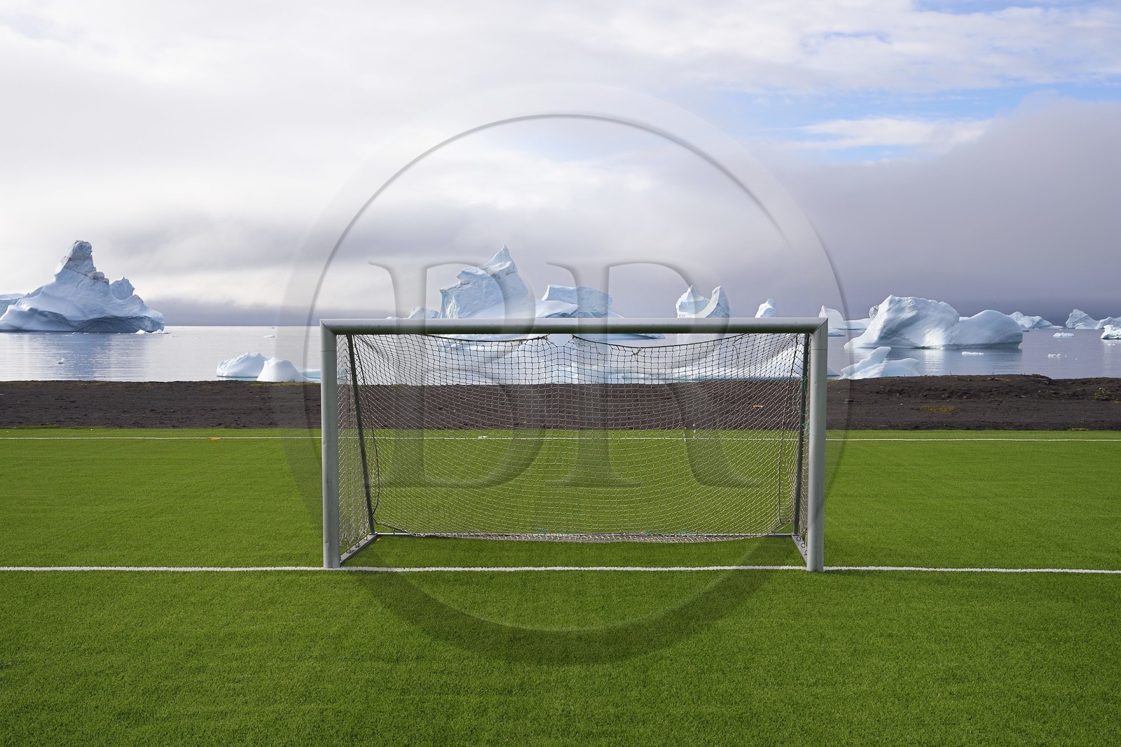 Greenland, west coast, Disko Island, Qeqertarsuaq, goal cage of a soccer field covered with synthetic grass and icebergs in the background