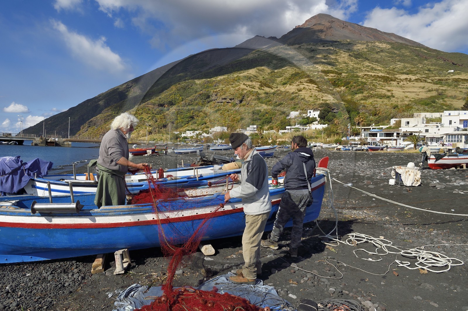 Italie, Sicile, iles Eoliennes, classées Patrimoine Mondial de l'UNESCO, ile de Stromboli, le pecheur Gaetano Cusolito réparant ses filets sur la plage de Scari et le volcan du Stromboli en arrière plan