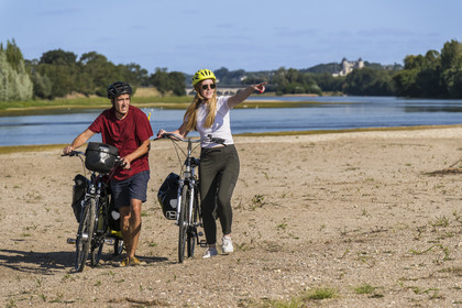 France, Maine-et-Loire, Loire valley listed as World Heritage by UNESCO, Saumur towards Saint-Hilaire, sandbanks forming islands on the Loire and Saumur castle in the background, cycling on the banks of the Loire, bike with a trailer carrying camping equipment
