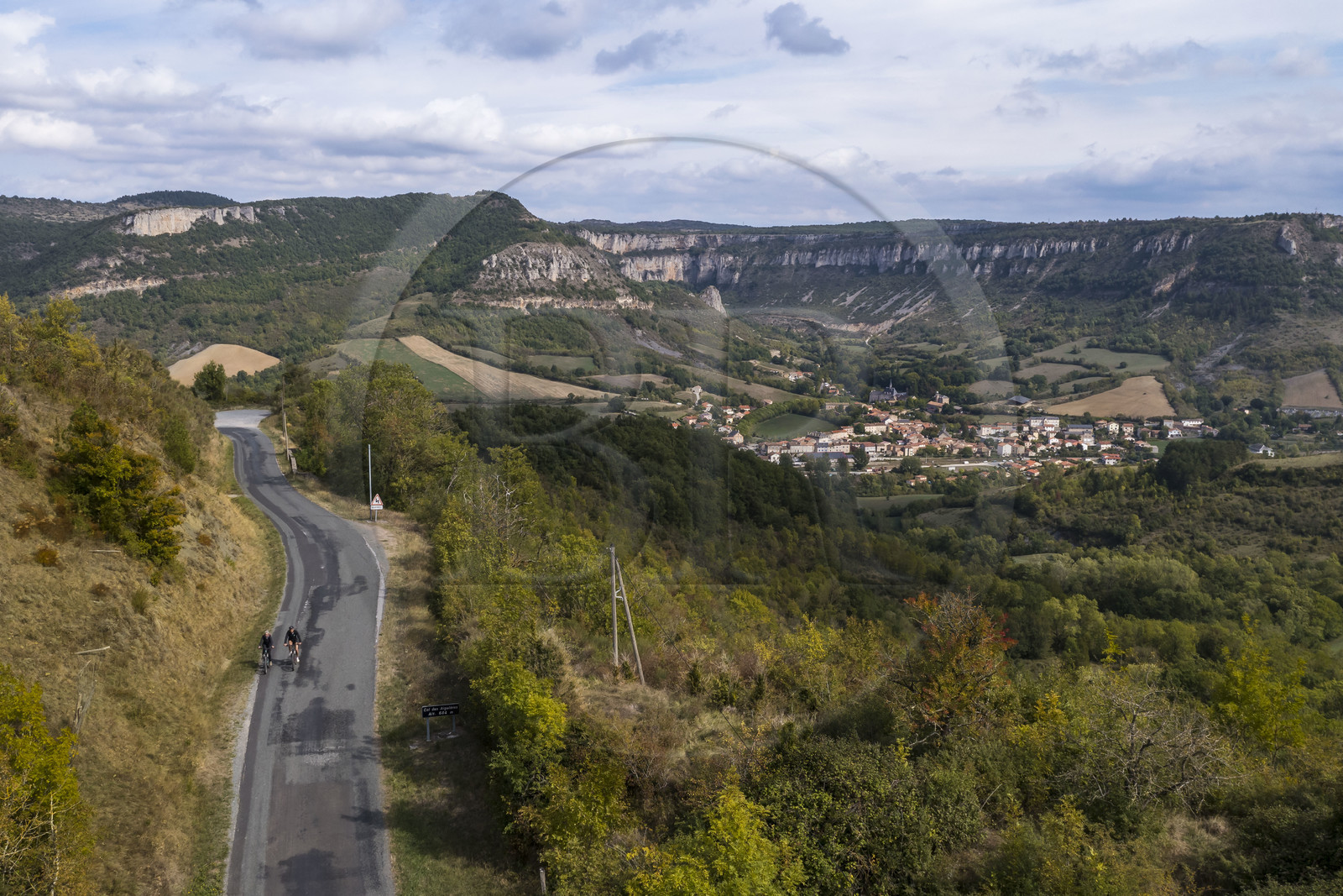 France, Aveyron, Grands-Causses Regional Nature Park, cyclistes effectuant l'itinéraire cyclo touristique Brebis'Cyclette en Pays de Roquefort, the village of Tournemire in the cirque at the foot of the Causse du Larzac (aerial view)