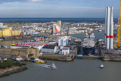 France, Loire-Atlantique, Saint-Nazaire, the fortified lock of the former German submarine base built during the last world war on the left and the construction site of the luxury super-yacht Ritz-Carlton Luminara in the Joubert dry dock on the right, the wind turbine towers are stored before embarkation (aerial view)