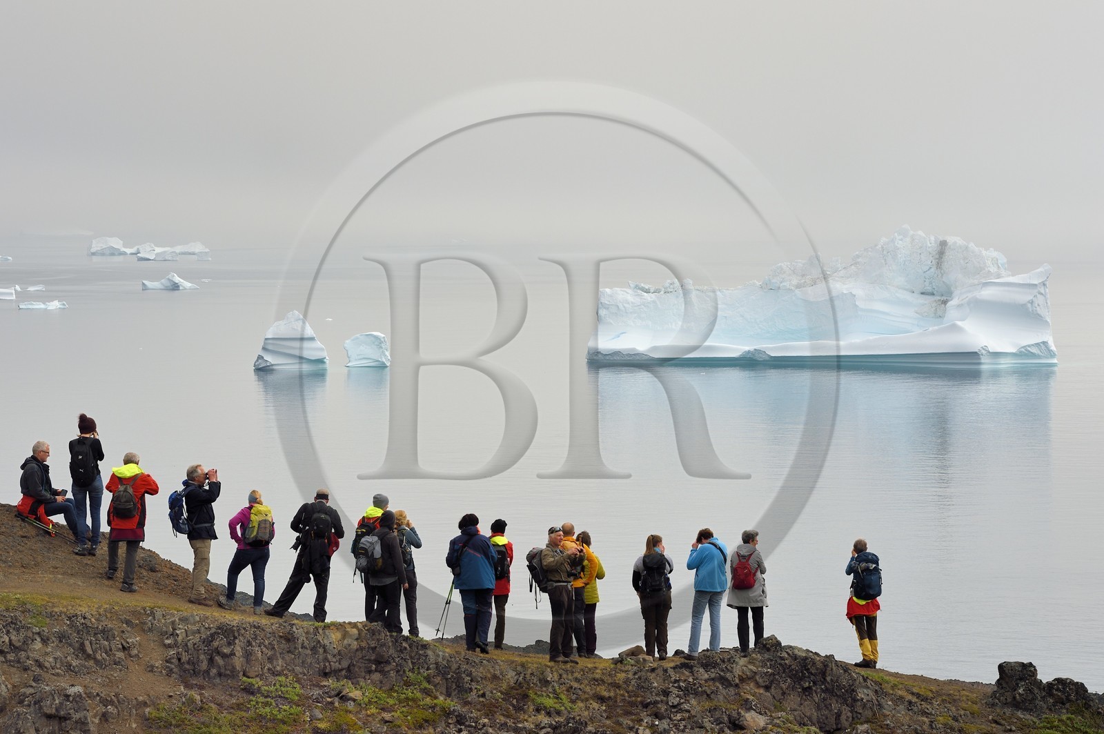 Groenland, cote ouest, Ile de Disko, Qeqertarsuaq, randonneurs sur la côte et icebergs dans la brume en arrière plan