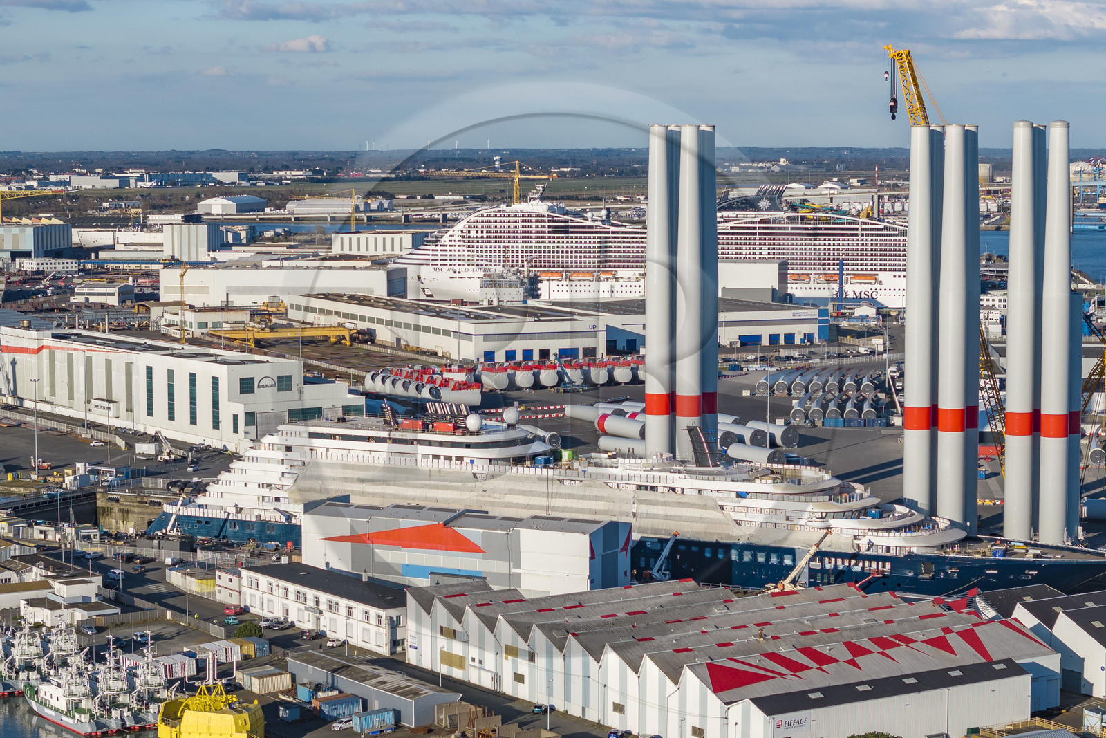 France, Loire Atlantique, Saint Nazaire, the construction site of the luxury super-yacht Ritz-Carlton Luminara in the Joubert dry dock in the foreground, the wind turbine towers are stored before embarkation, the 333m MSC World America cruise ship built by Chantiers de l'Atlantique in the background (aerial view)