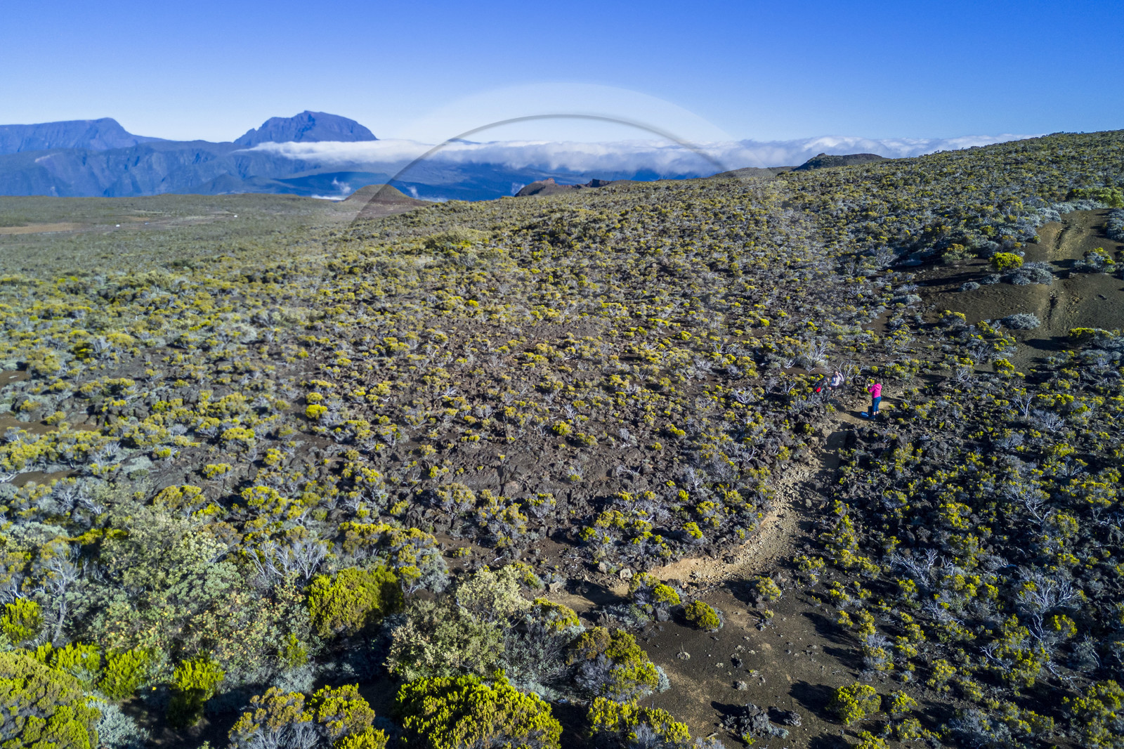 France, Ile de la Reunion, Parc National de la Réunion classé Patrimoine Mondial de l'UNESCO, sur les pentes du volcan de Piton de la Fournaise, randonneur sur le sentier de l'oratoire Ste Thérèse au dessus de la Plaine des Sables, le Piton des Neiges en arrière plan au nord (vue aérienne)