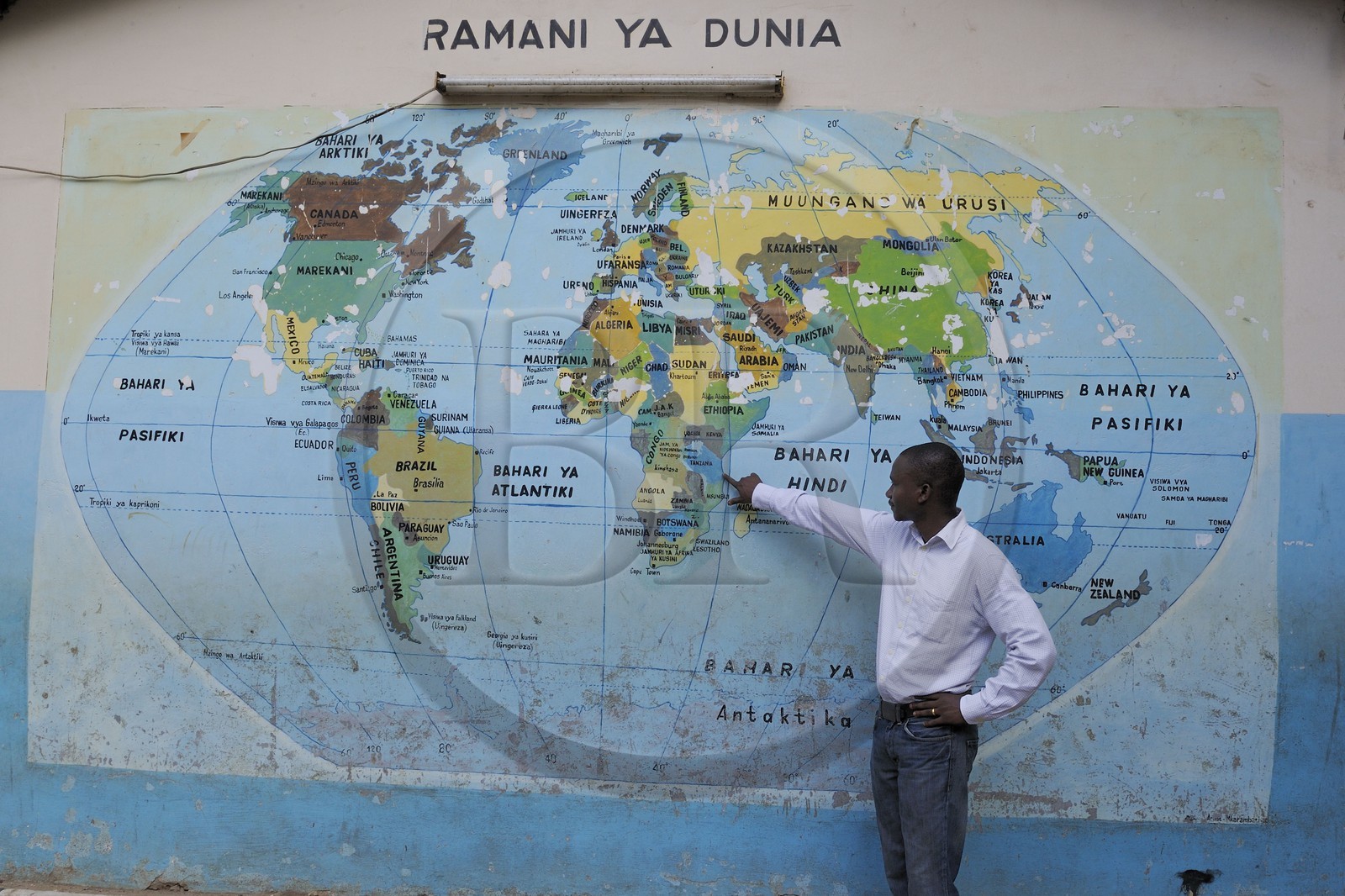 Tanzanie, Dar es-Salaam, Joseph Malumbo pointe la Tanzanie sur la mappemonde murale dessinée sur le mur d'entrée de son ancienne école du quartier de Kivukoni