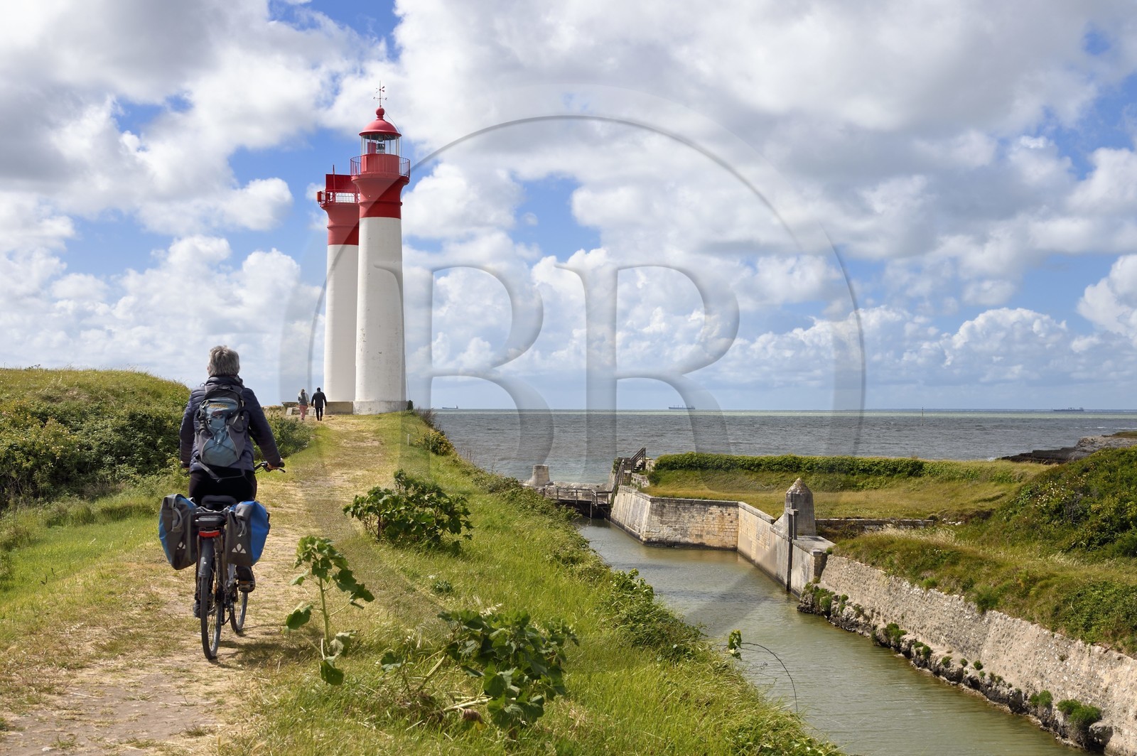 France, Charente-Maritime, Ile d'Aix (Aix Island), Fort de la Rade, lighthouse of the island with two towers built in 1840 and ditches of the fortifications on the right, cyclist traveling along the Flow Vélo cycle route