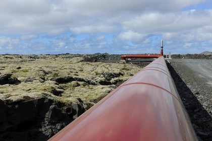 Iceland, Sudurnes Region, Grindavik, the Blue Lagoon with drains and lava in the foreground and the geothermical factory in the background