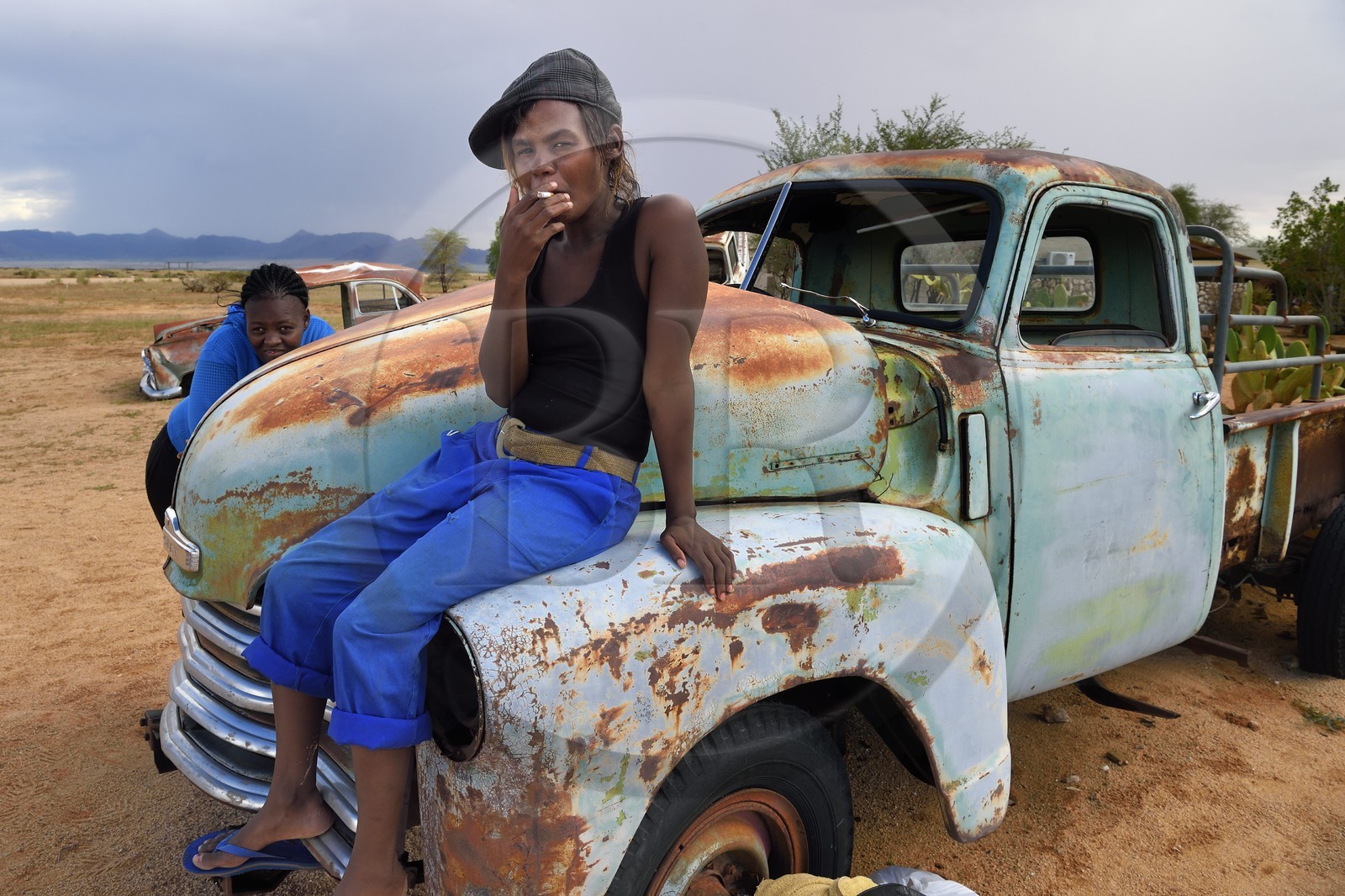 Namibie, région de Khomas, désert du Namib à l'Est du parc national Namib Naukluft, station essence de Solitaire, Gloria une jeune routarde namibienne qui fait la route assise sur la carcasse d'un pick-up Chevrolet