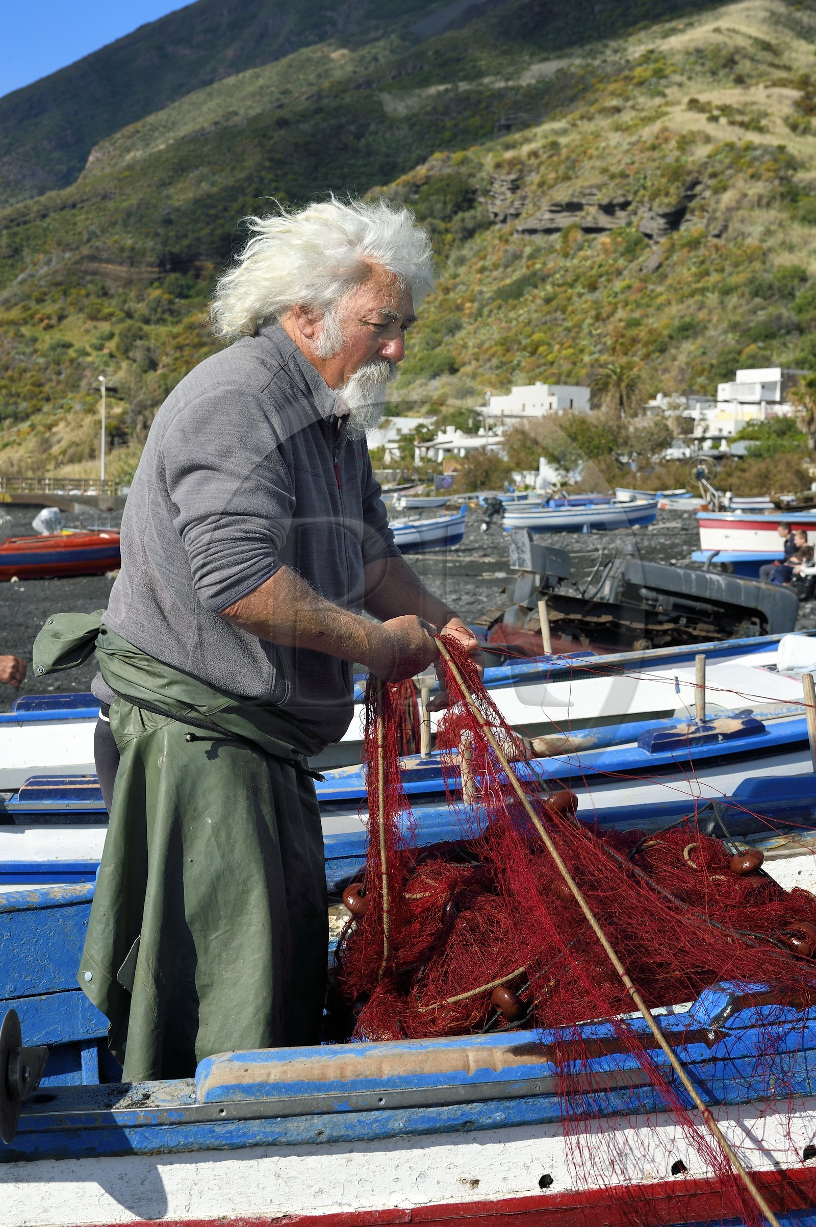 Italie, Sicile, iles Eoliennes, classées Patrimoine Mondial de l'UNESCO, ile de Stromboli, le pecheur Gaetano Cusolito réparant ses filets sur la plage de Scari et le volcan du Stromboli en arrière plan