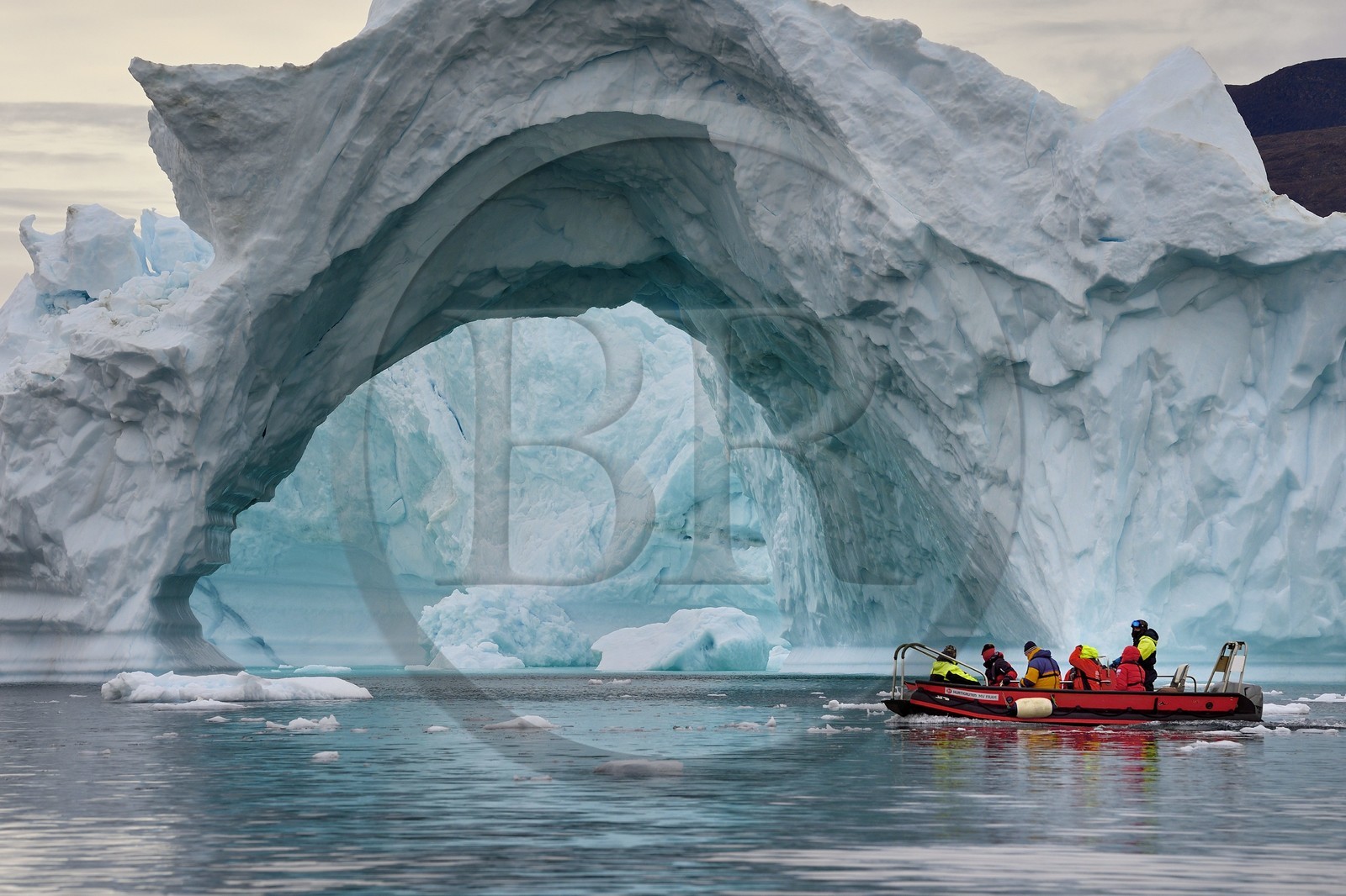 Greenland, North West coast, Baffin Sea, Inglefield Fjord towards Qaanaaq, iceberg forming an arch and an exploration PolarCirkel boat (zodiac) of the MS Fram cruse ship from Hurtigruten