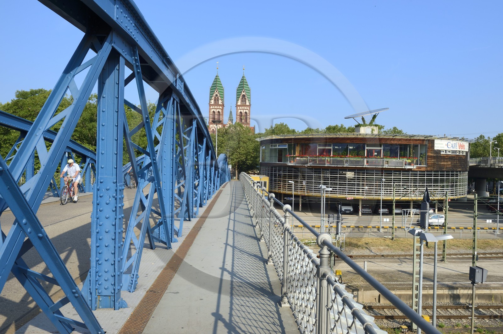 Germany, Baden-Wurttemberg, Freiburg im Breisgau, cyclist on the blue bridge (wiwili-bridge), the Sacred Heart of Jesus Church (Herz-Jesu-kirche) and the Bicycle station called Mobile at the Central Station in the background
