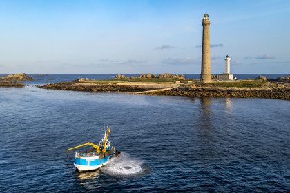 France, Finistère, Abers Country (Pays des Abers), Ile Vierge (Virgin Island) in the Lilia archipelago, seaweed boat using one of its two articulated mechanical arms ending in a scoubidou to harvest seaweed, the Virgin Island lighthouse in the background (aerial view)