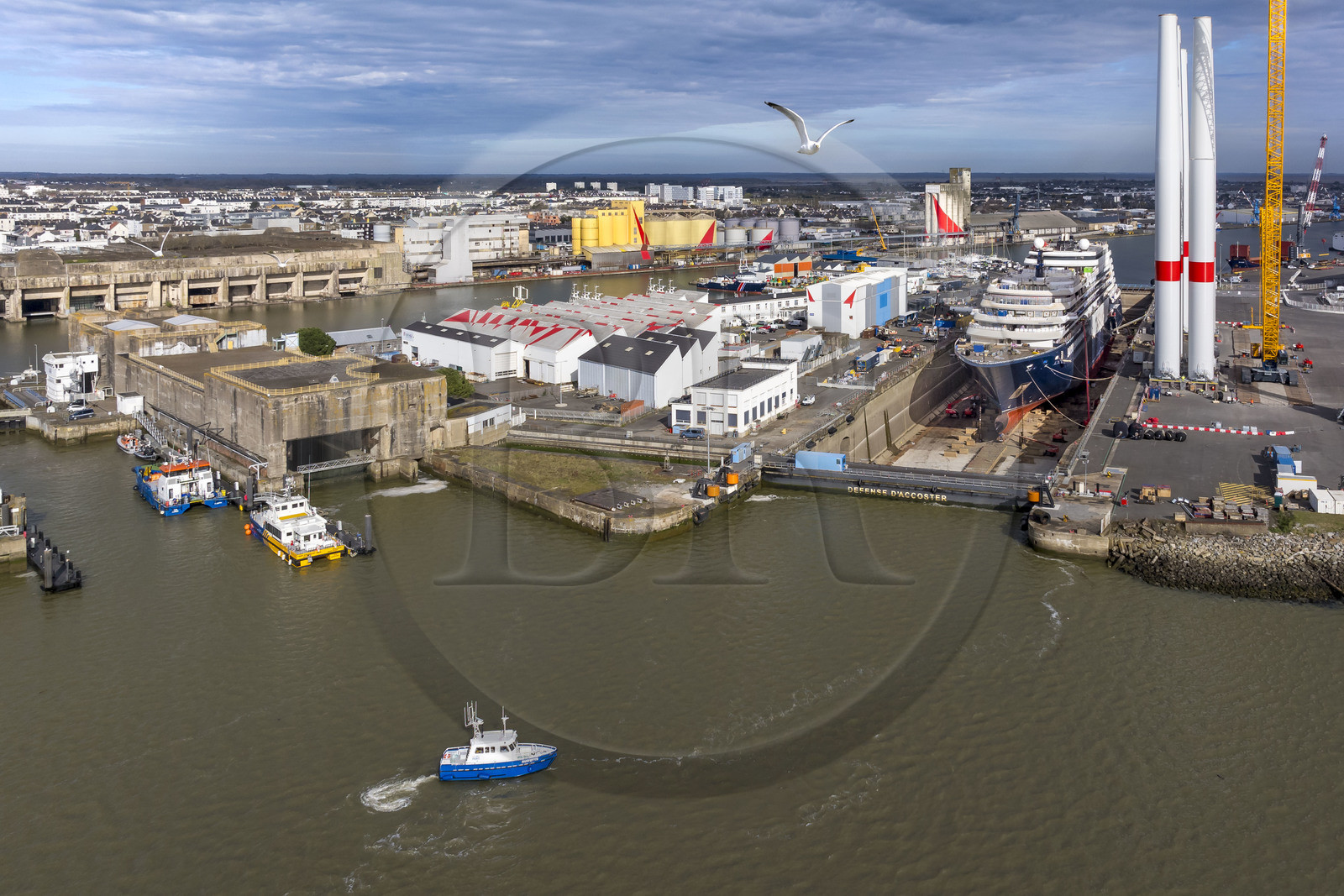 France, Loire-Atlantique, Saint-Nazaire, the former German submarine base and fortified lock built during the last world war on the left and the construction site of the luxury super-yacht Ritz-Carlton Luminara in the Joubert dry dock on the right, the wind turbine towers are stored before embarkation (aerial view)