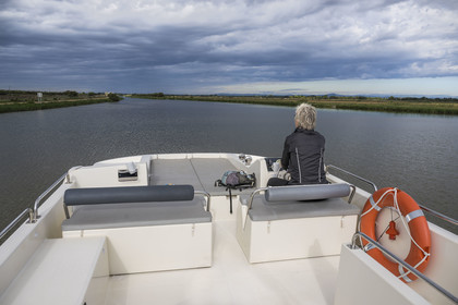 France, Gard, Aigues-Mortes, navigation of a pleasure boat Le Boat on the Rhone to Sète Canal out of town, the Portes de Vidourle in the background