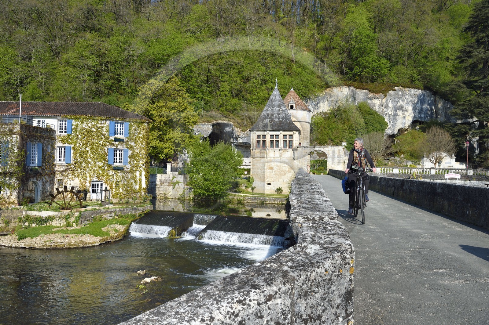 France, Dordogne, Brantome, Pont Coude (angled bridge) over Dronne River and the Moulin de L'Abbaye left, former 14th century mill transformed into Hotel ****, the Renaissance pavilion and the tower which formed the fortified gate in the background, cyclists on the Flow Vélo cycle route