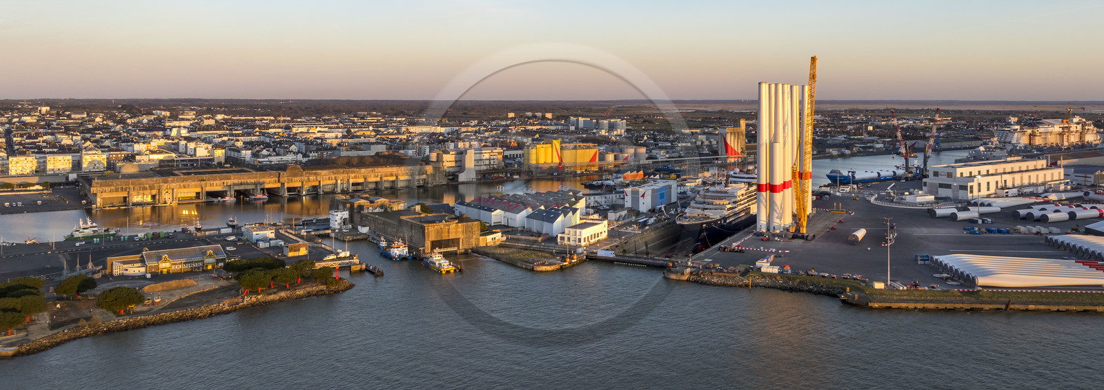 France, Loire-Atlantique (44), Saint-Nazaire, l'ancienne base sous-marine allemande construite lors de la dernière guerre mondiale borde le bassin à flot du port de Saint-Nazaire,  l’écluse Est et l'écluse fortifiée au premier plan et le chantier du super-yacht de luxe Ritz-Carlton Luminara dans la forme Joubert à droite, les tours d'éoliennes sont stockées avant embarquement (vue aérienne)