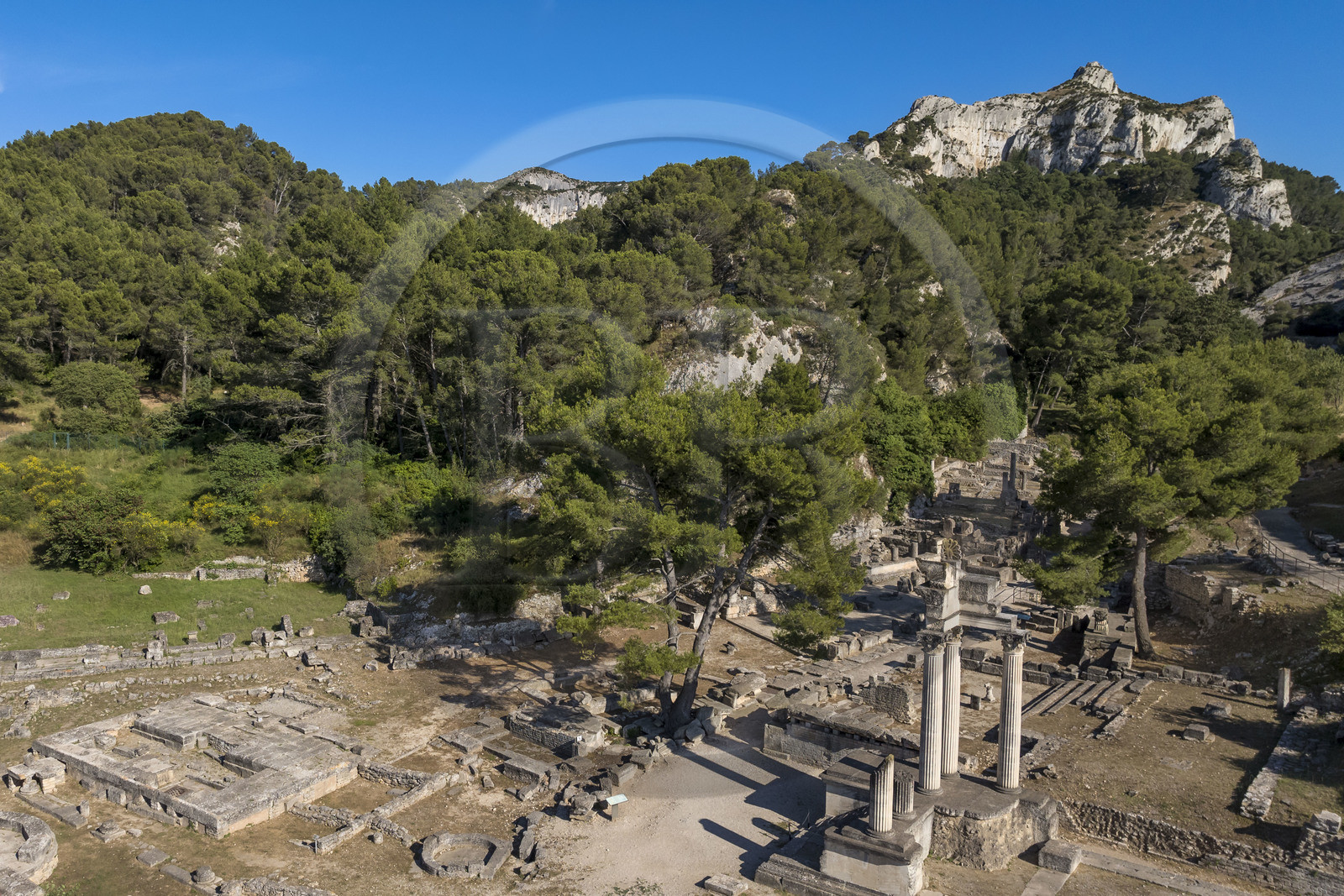 France, Bouches-du-Rhône (13), Parc Naturel Régional des Alpilles, Saint-Rémy-de-Provence, site archéologique de Glanum au pied du massif des Alpilles, colonnes et entablement reconstitués du petit temple géminé du premier forum au premier plan à droite (vue aérienne)