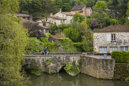 France, Vendée (85), Vouvant, labellisé Les Plus Beaux Villages de France, cycliste traversant le petit pont médiéval sur la rivière La Mère qui entoure le village