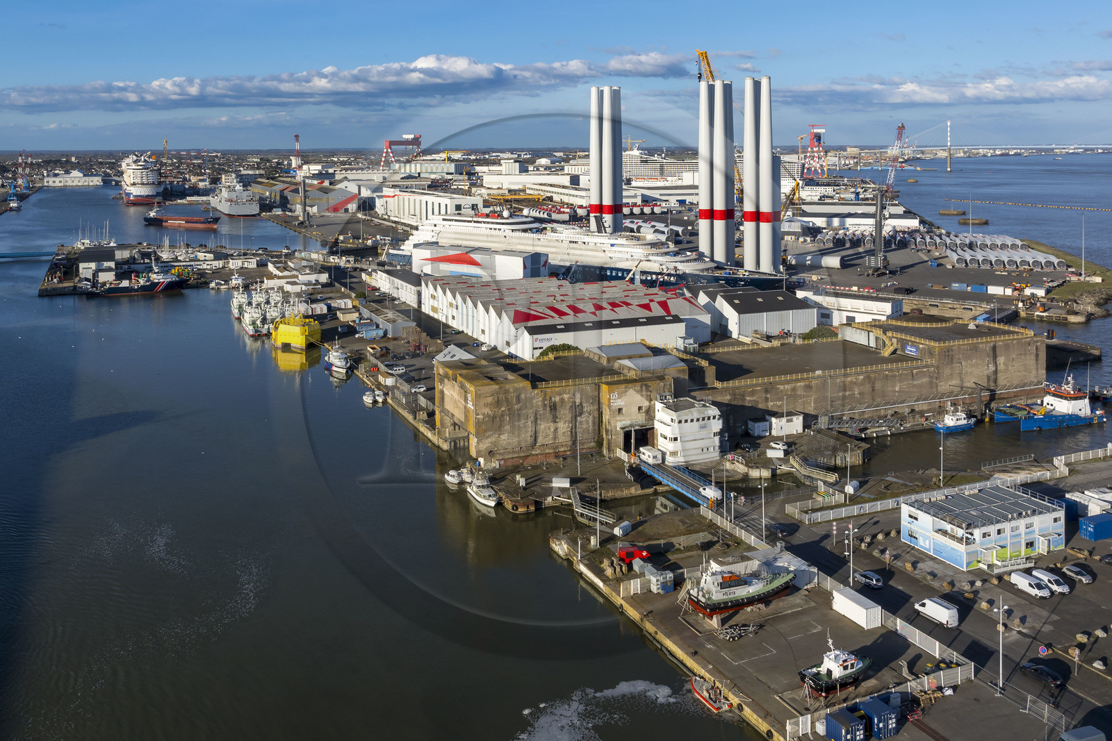 France, Loire-Atlantique (44), Saint-Nazaire, l’écluse Est et l'écluse fortifiée de l'ancienne base sous-marine allemande construite lors de la dernière guerre mondiale au premier plan et le chantier du super-yacht de luxe Ritz-Carlton Luminara dans la forme Joubert, les tours d'éoliennes en arrière plan sont stockées avant embarquement (vue aérienne)