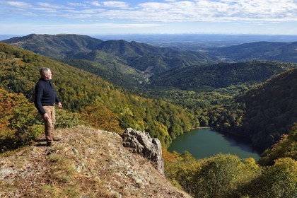 France, Vosges, Ballons des Vosges Regional Natural Park, Saint Maurice sur Moselle, hiker at the Tete des Perches mountain peak over Gazon Rouge, the Lac des Perches, the plain of Alsace and the Alps in the background